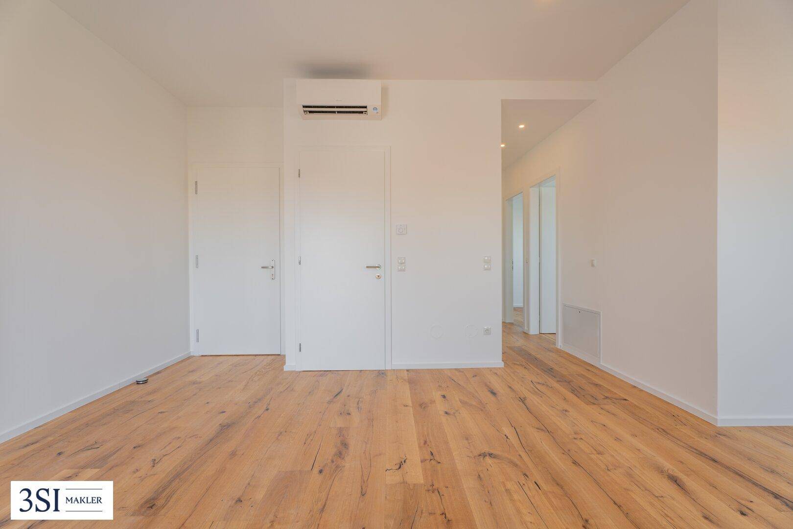 Heller Raum mit Holzboden, zwei Türen und einer Klimaanlage an der Wand.