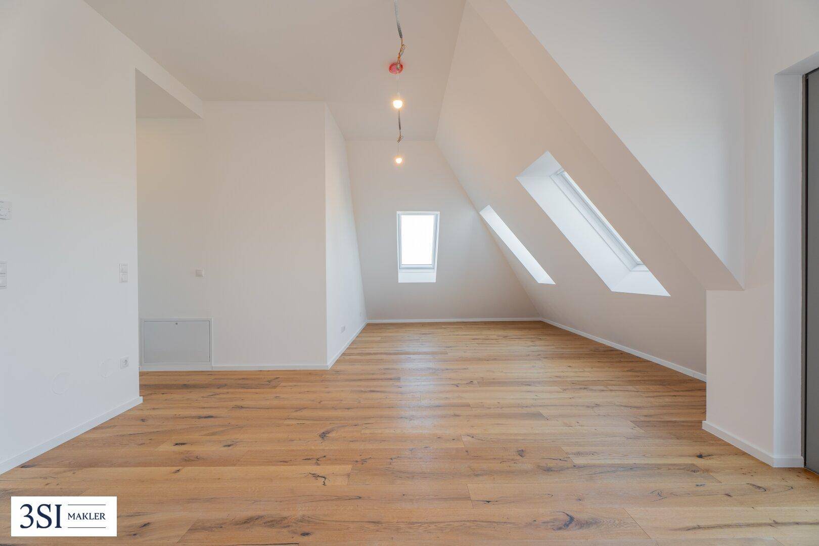 Geräumiges Dachgeschosszimmer mit schrägen Wänden, Holzboden und mehreren Dachfenstern.