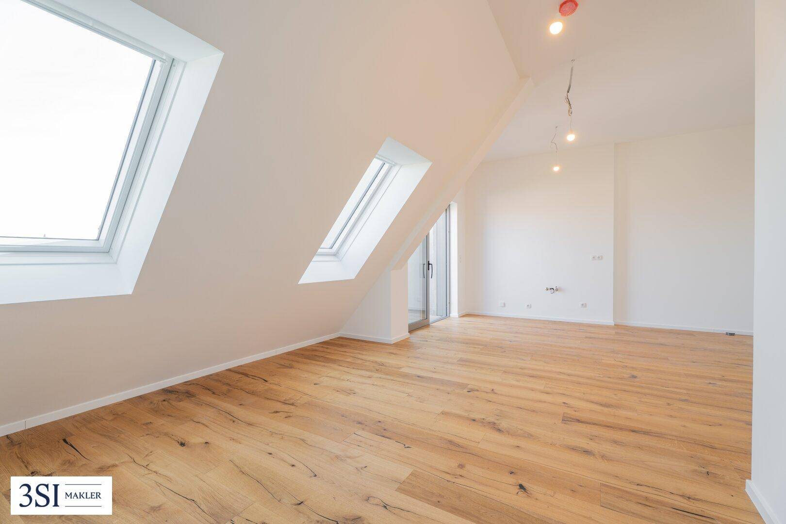 Lichtdurchflutetes Zimmer mit Holzboden, großen Dachfenstern und Zugang zum Balkon.