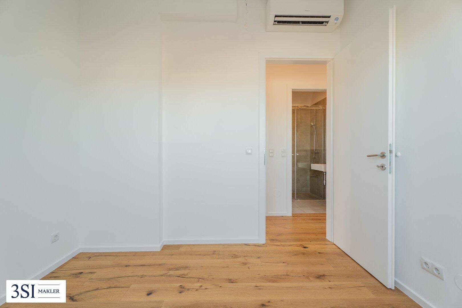 Schlafzimmer mit Holzboden, Klimaanlage und direktem Zugang zu einem modernen Badezimmer.