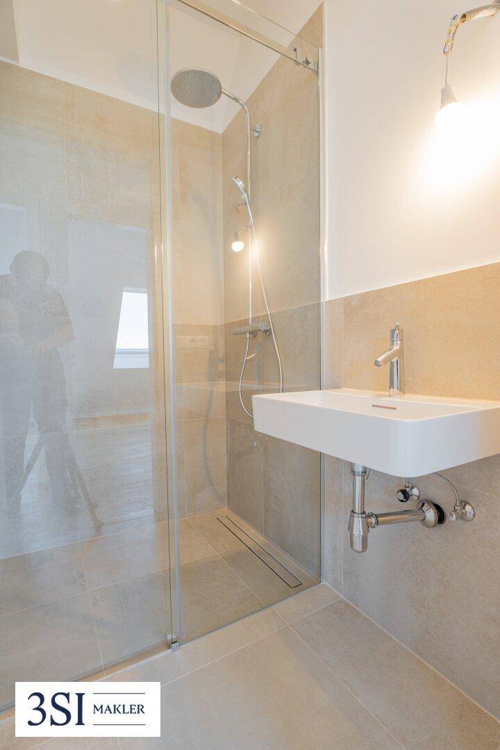 Modernes Badezimmer mit beigefarbenen Fliesen, wandhängendem Waschbecken und begehbarer Regendusche.