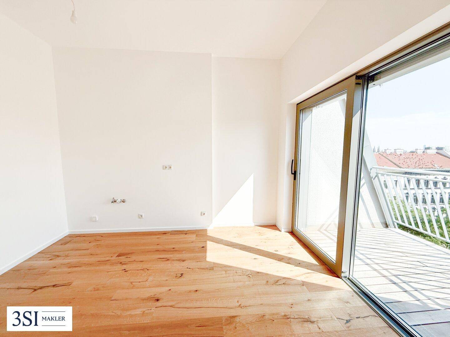 Lichtdurchfluteter Raum mit Holzboden und breiter Schiebetür, die auf einen sonnigen Balkon führt.