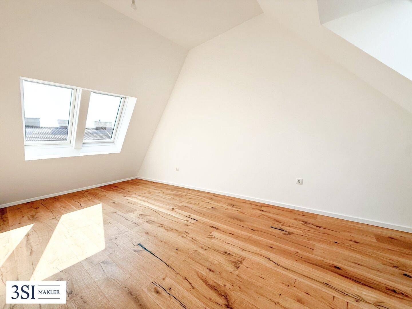 Geräumiger Raum mit Holzboden, weißen Wänden und zwei Dachfenstern, die viel Tageslicht hereinlassen.