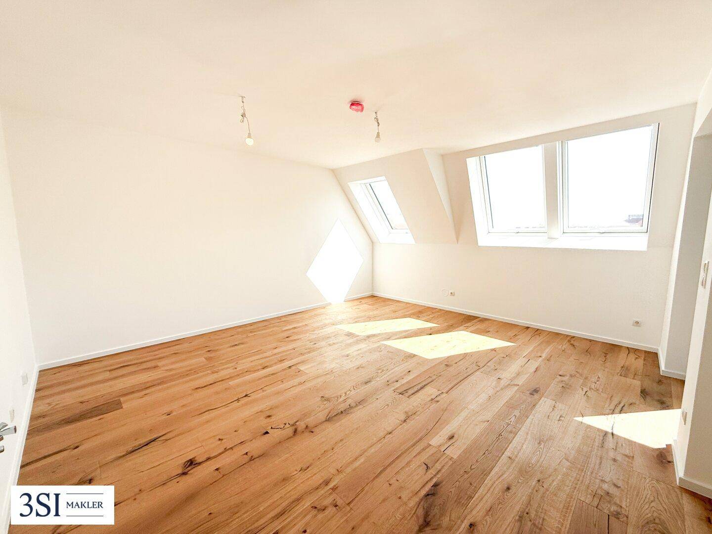 Lichtdurchflutetes Zimmer im Dachgeschoss mit Holzboden und Dachfenstern, bietet eine gemütliche Atmosphäre.