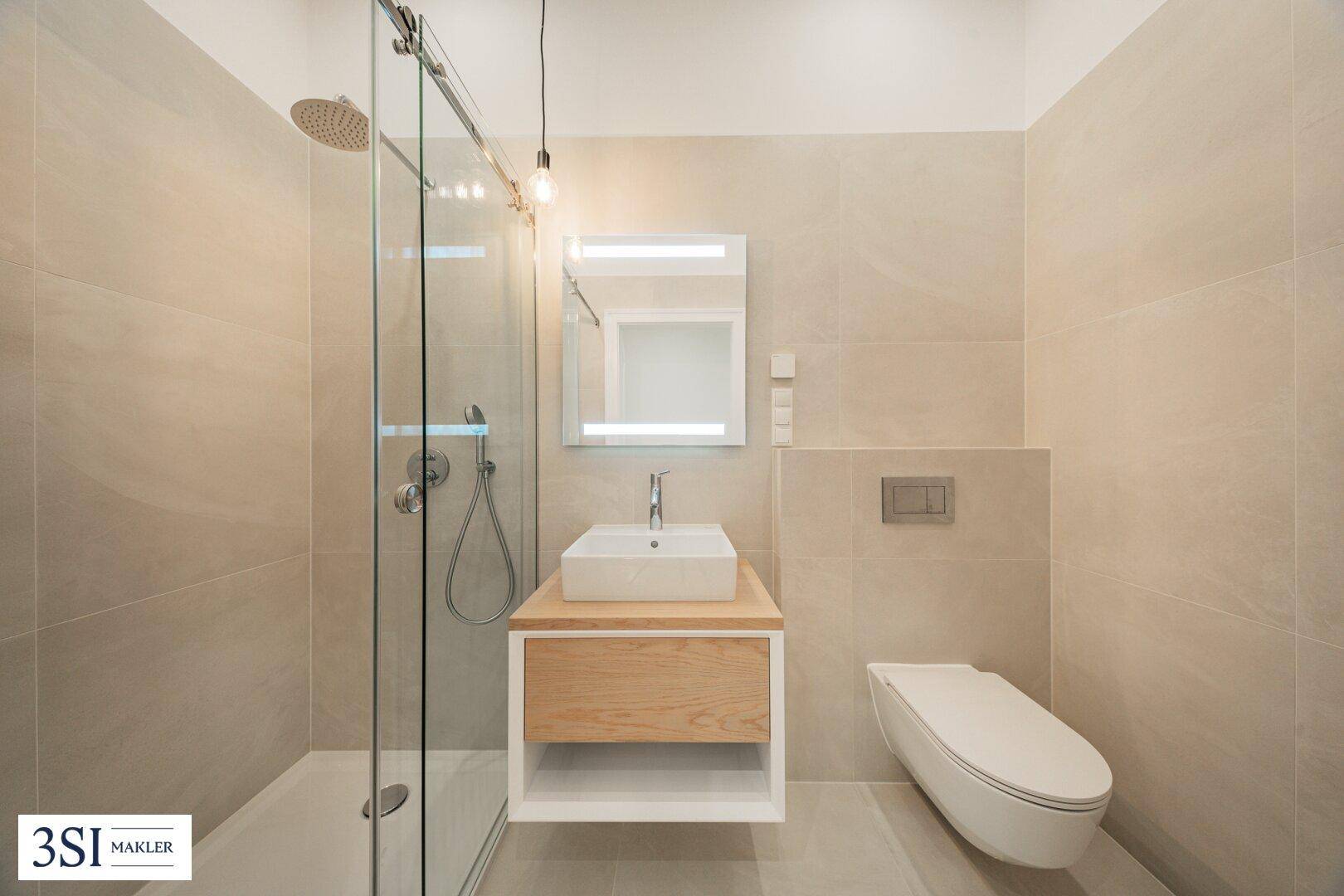 Modernes Badezimmer mit begehbarer Dusche, Einzelwaschbecken und wandhängendem WC in hellen Beigetönen.