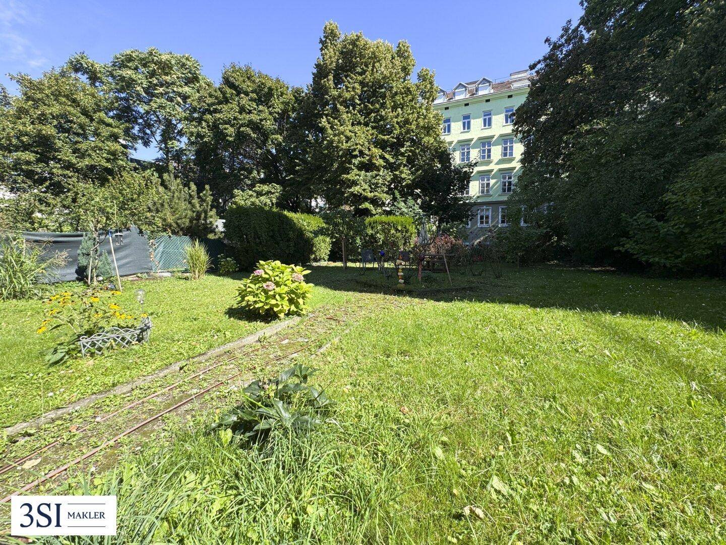 Grüner Gartenbereich mit altem Baumbestand und Rasenfläche hinter einem Wohngebäude.