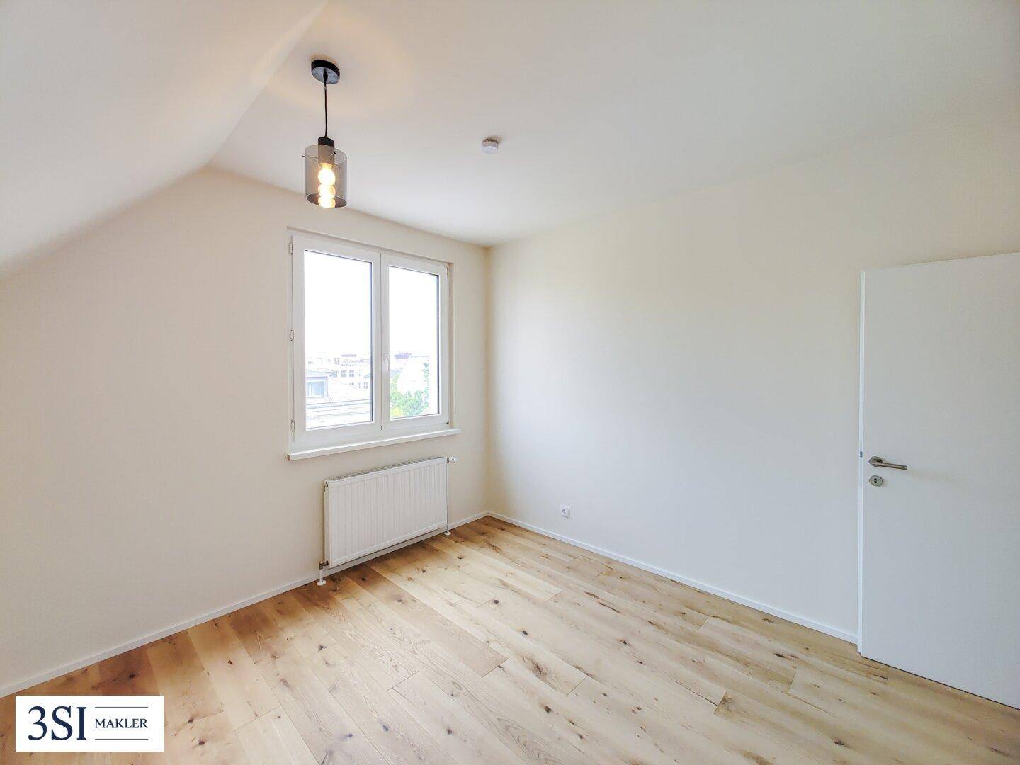 Schlafzimmer mit hellem Parkettboden, weiß gestrichenen Wänden und Fenster.