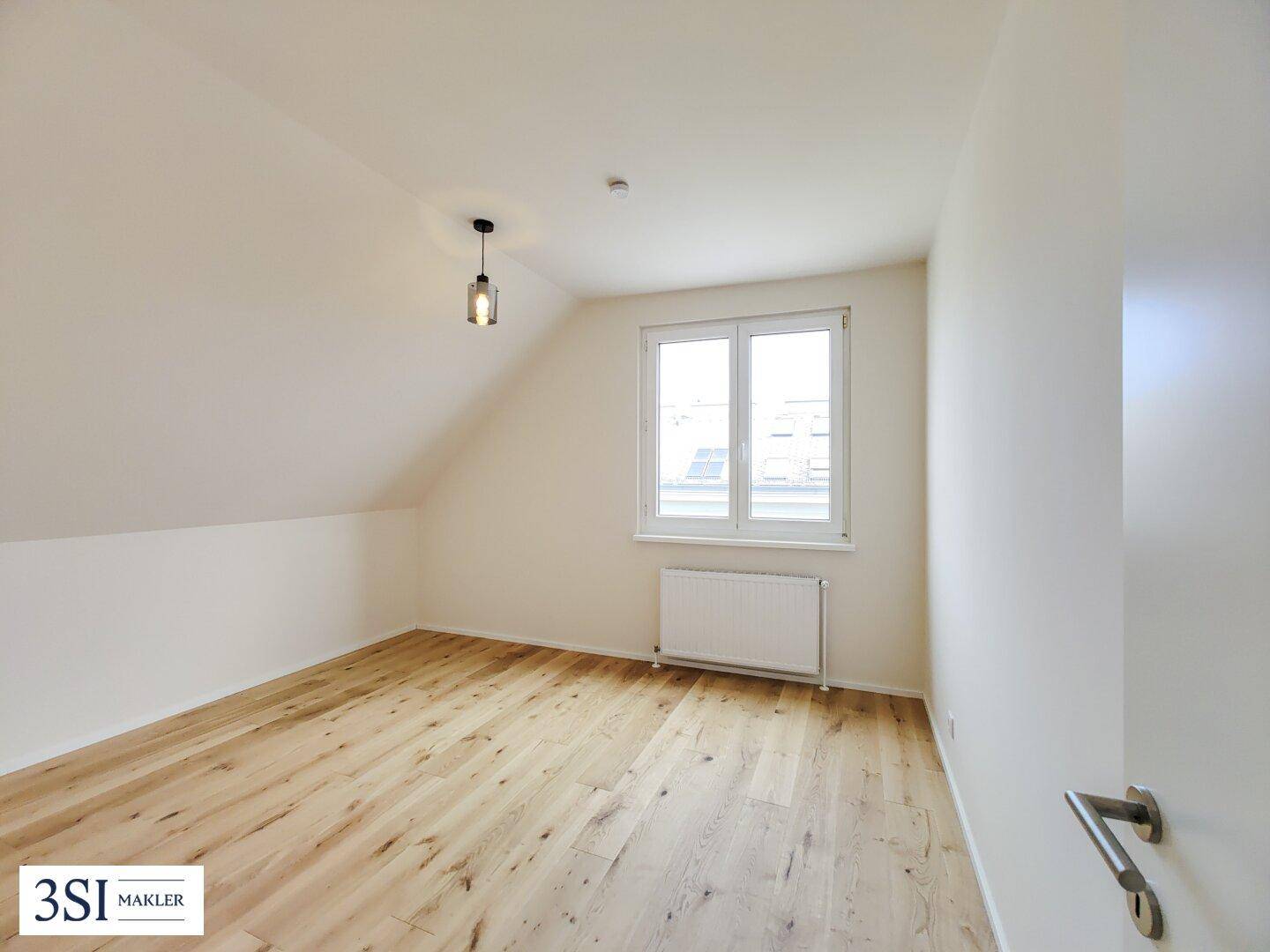 Helles Schlafzimmer mit Parkettboden, Dachschräge und Fenster.