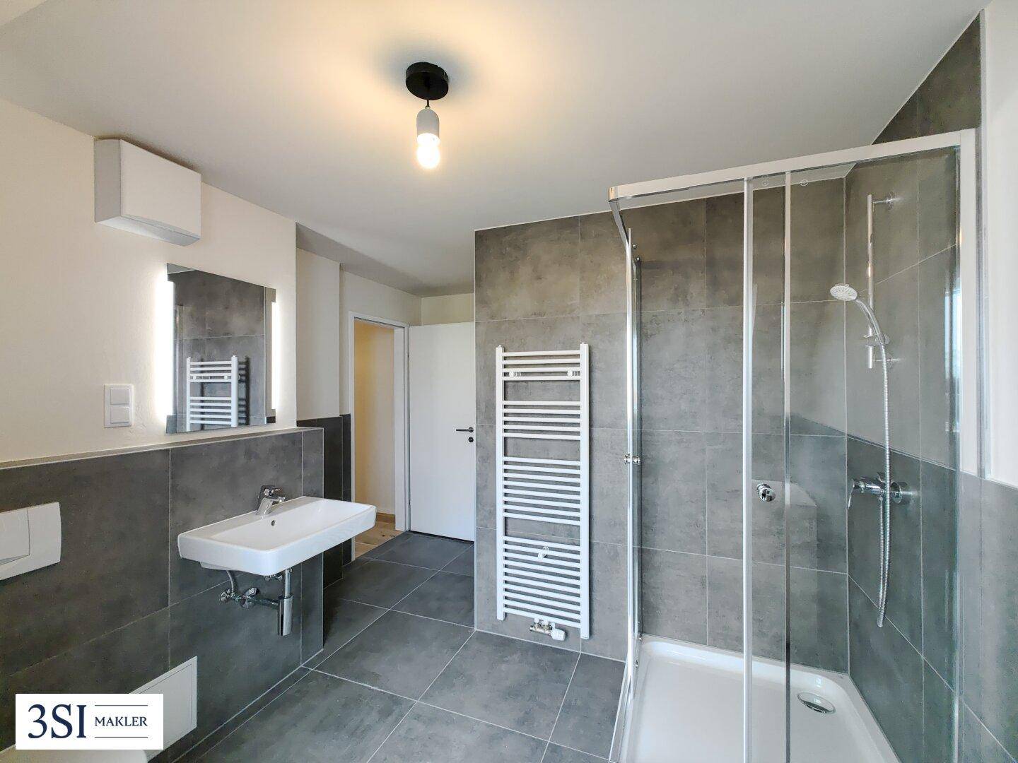 Modernes Badezimmer mit grauen Fliesen, Dusche, Waschbecken und Handtuchheizkörper.