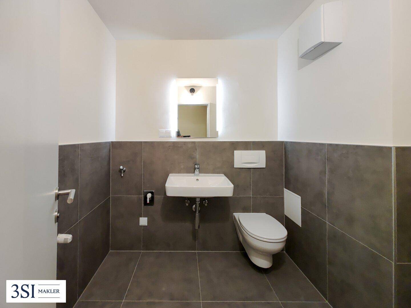 Modernes Gäste-WC mit grauen Fliesen, Waschbecken und wandhängendem WC.