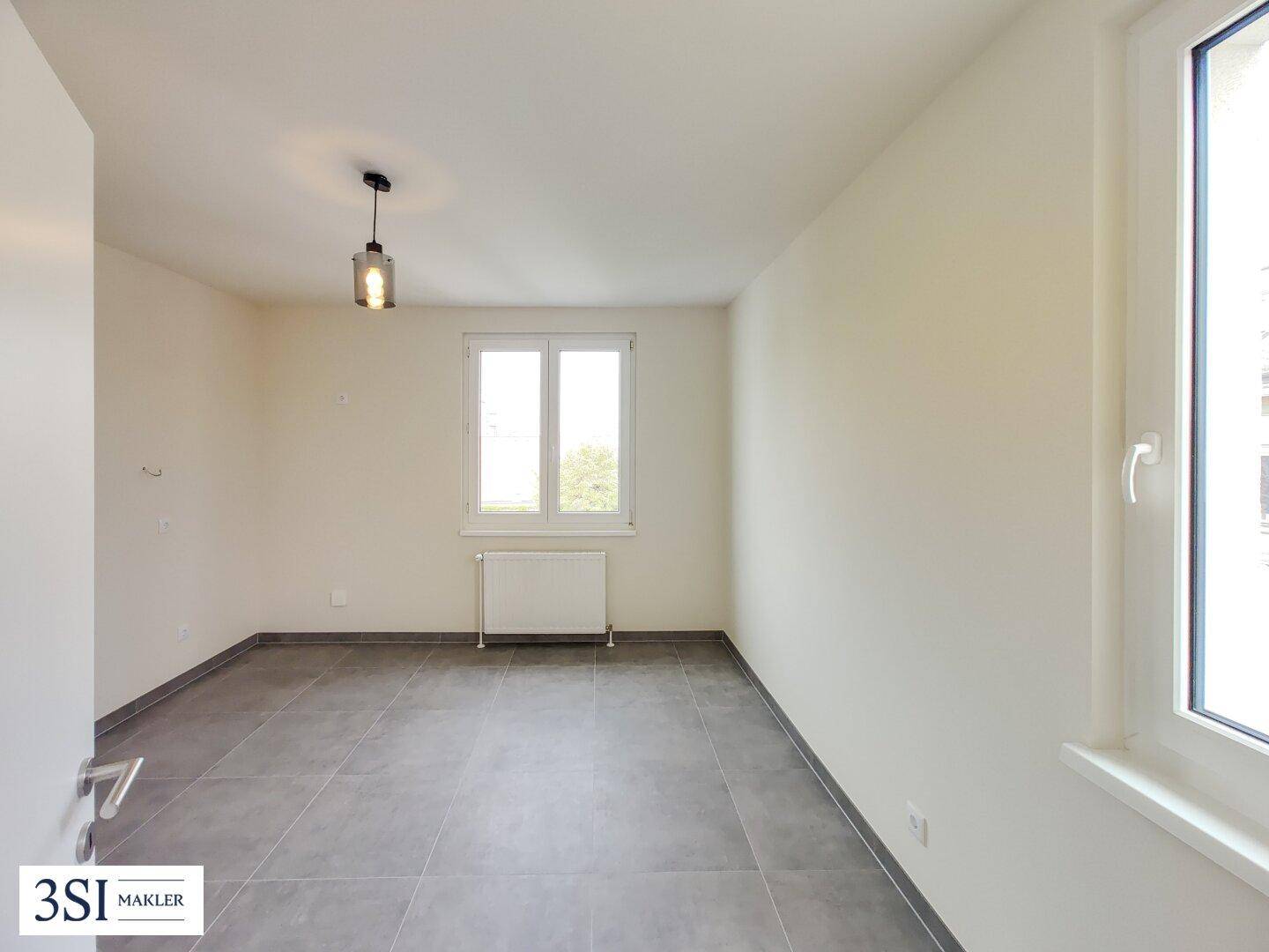 Schlichtes Zimmer mit grauen Fliesen, weiß gestrichenen Wänden und Fenster.