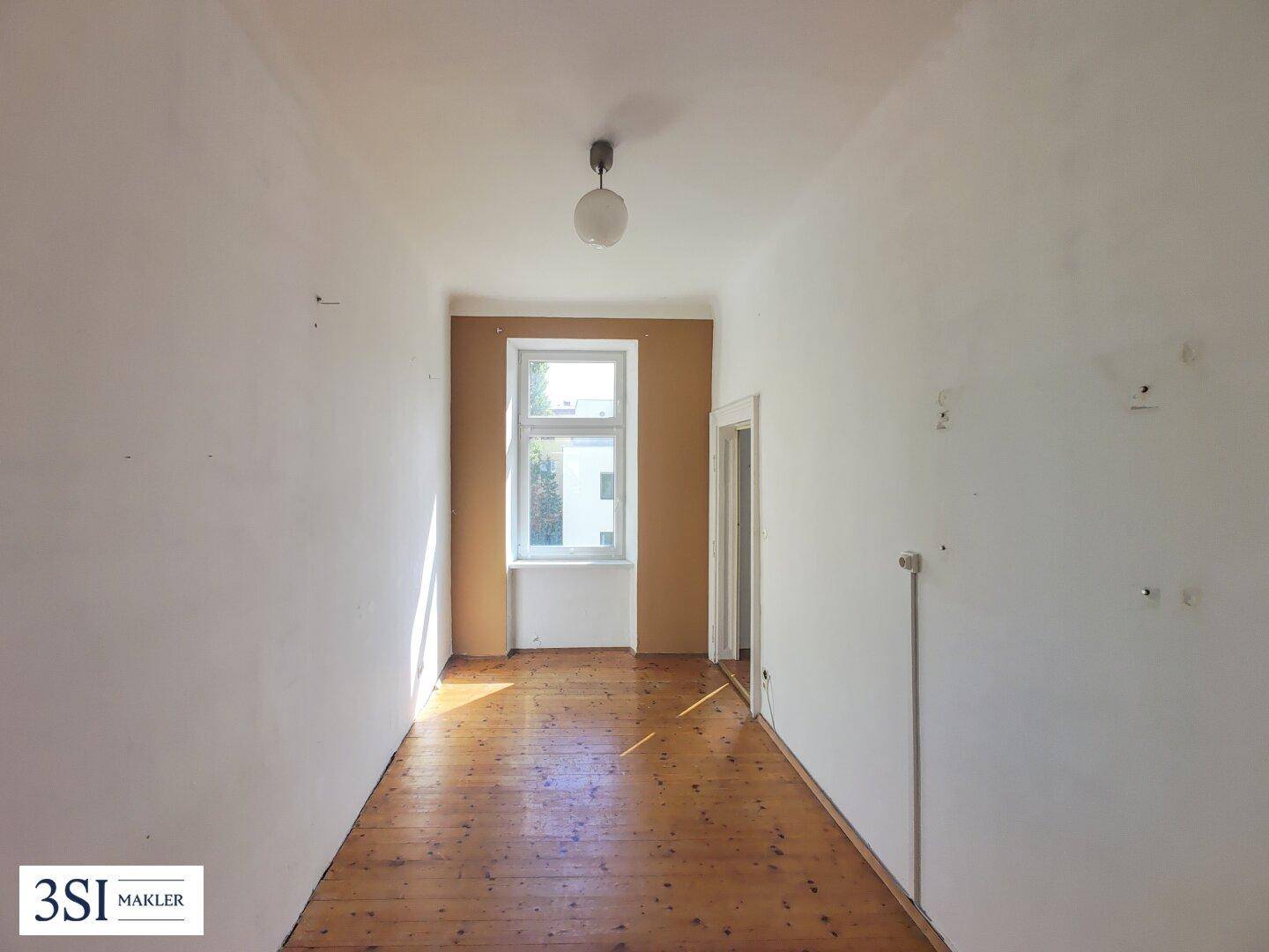 Langer, leerer Raum mit Holzdielenboden und einem Fenster, ideal für ein Schlafzimmer.