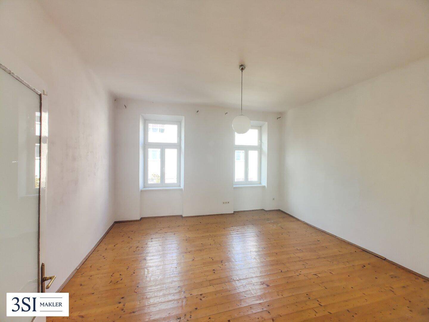Leerer Raum mit Holzdielenboden und zwei Fenstern, bereit zur individuellen Gestaltung.