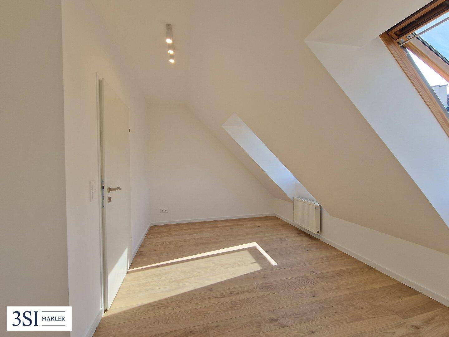 Lichtdurchfluteter Raum im Dachgeschoss mit hellem Holzboden, Dachfenster und charakteristischen Schrägen.