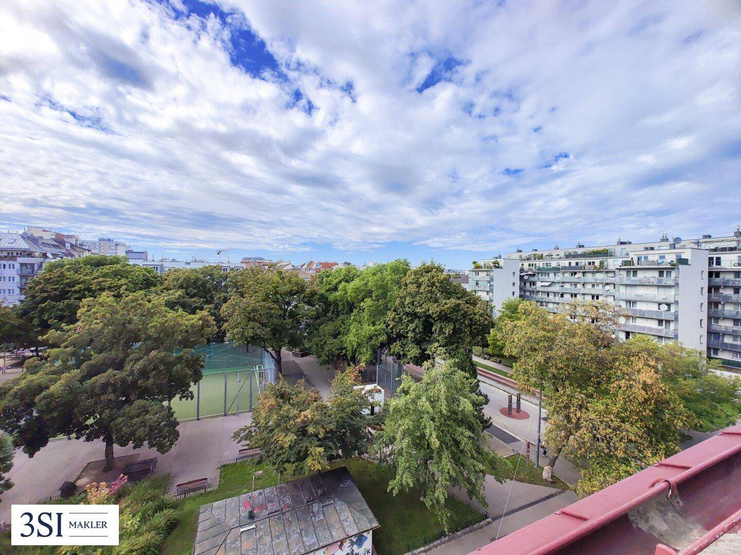 Weitläufiger Blick von oben auf eine grüne Parkanlage mit Sportplatz und städtischer Bebauung.