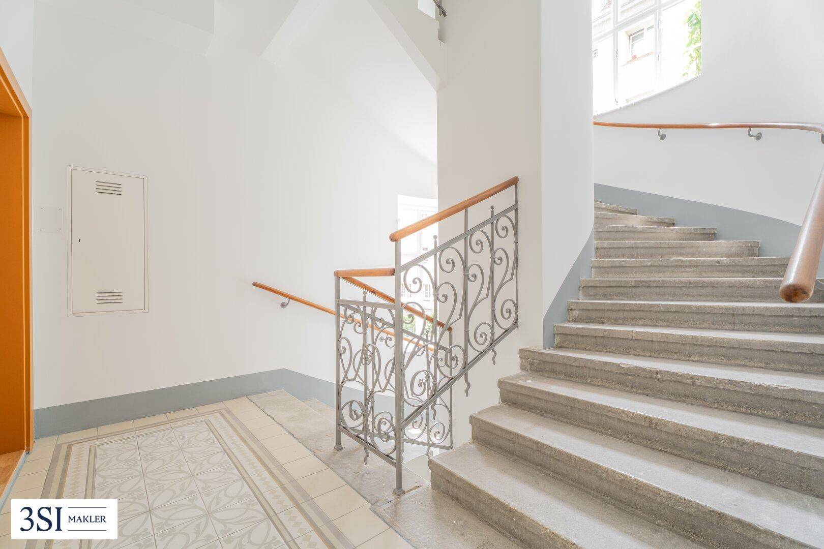 Historisches Treppenhaus mit Steinstufen, kunstvollem Geländer und Holzhandlauf in einem Altbau.