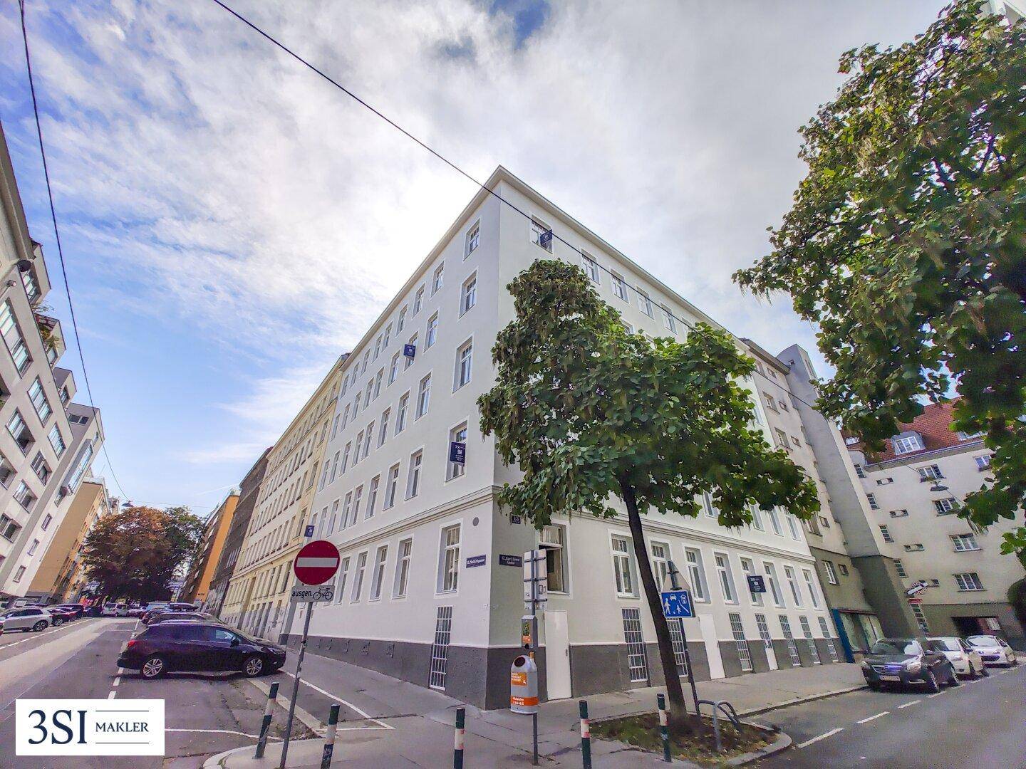 Weitläufige Außenansicht eines Eckgebäudes in einer belebten Stadtstraße mit umliegenden Gebäuden.