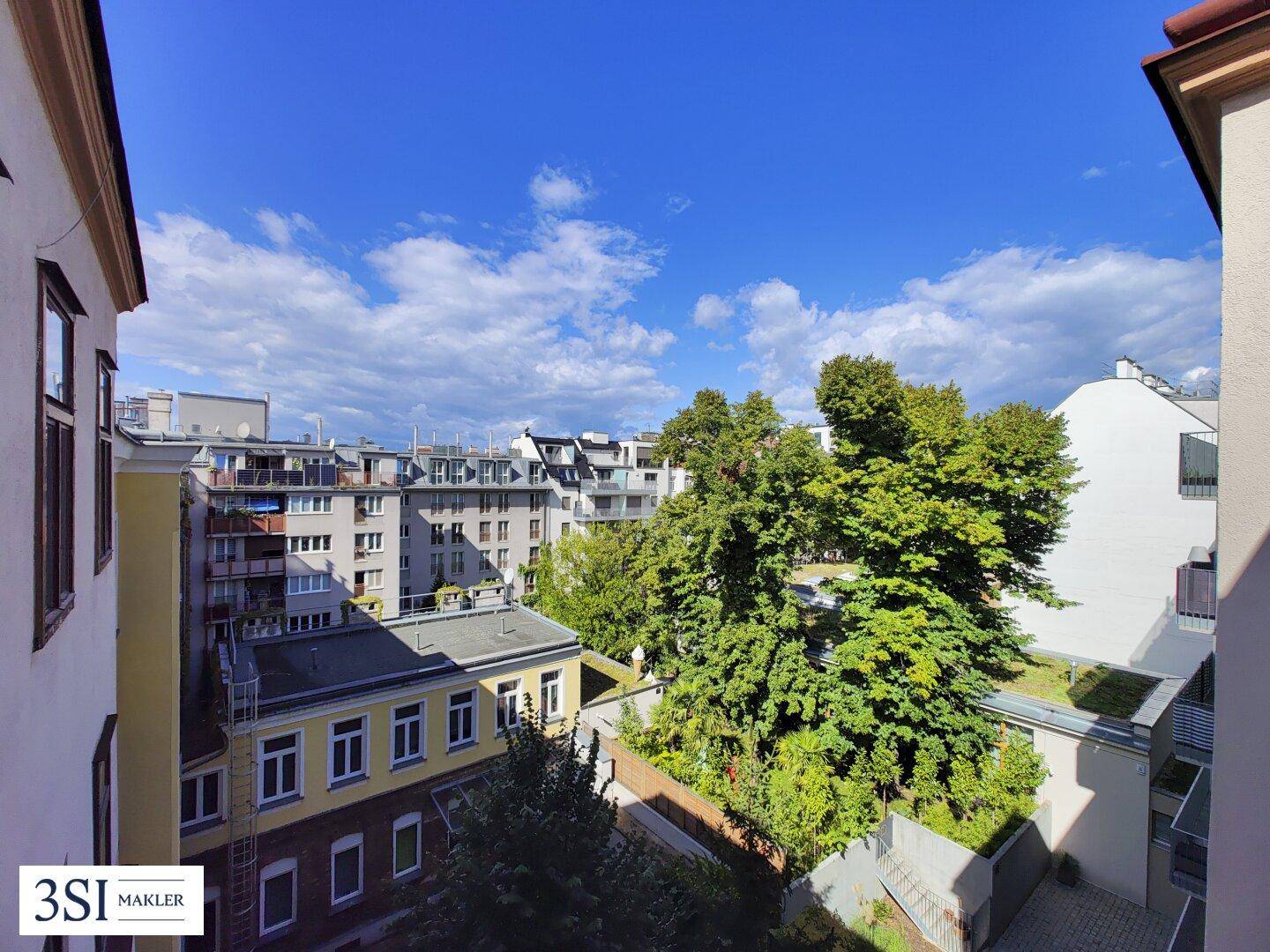 Blick in einen begrünten Innenhof mit Bäumen und umliegenden Gebäuden.