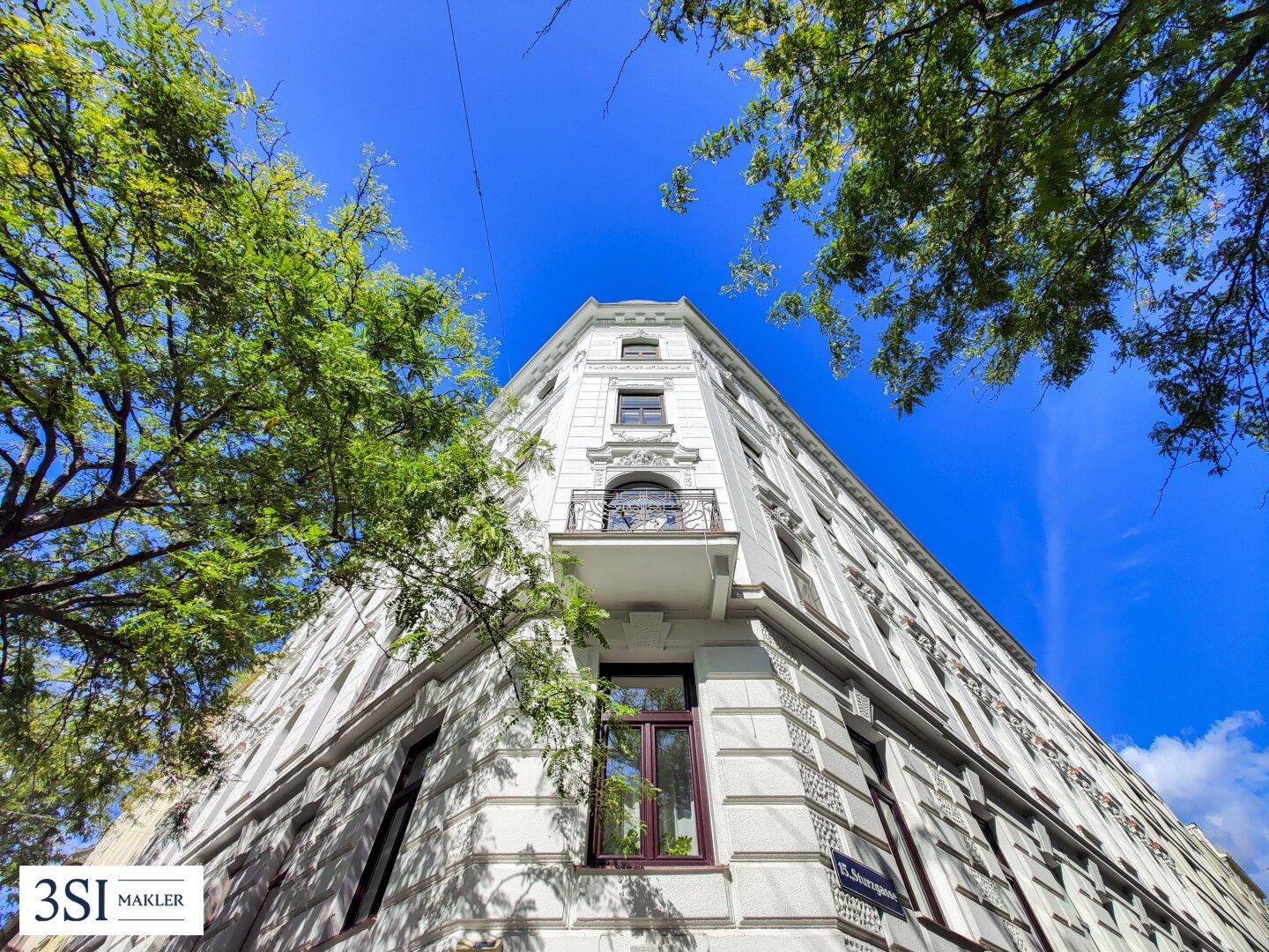 Blick von unten auf die historische Fassade des Eckgebäudes mit kleinem Balkon.