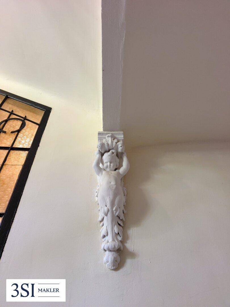 Detailaufnahme einer Stuckverzierung in Form einer Figur an der Wand.