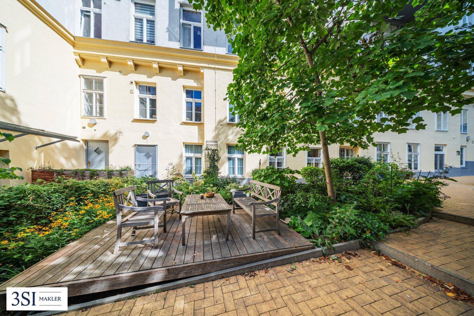 Gemütlicher Außenbereich im Innenhof mit Holzdeck und Sitzgelegenheiten unter Bäumen.