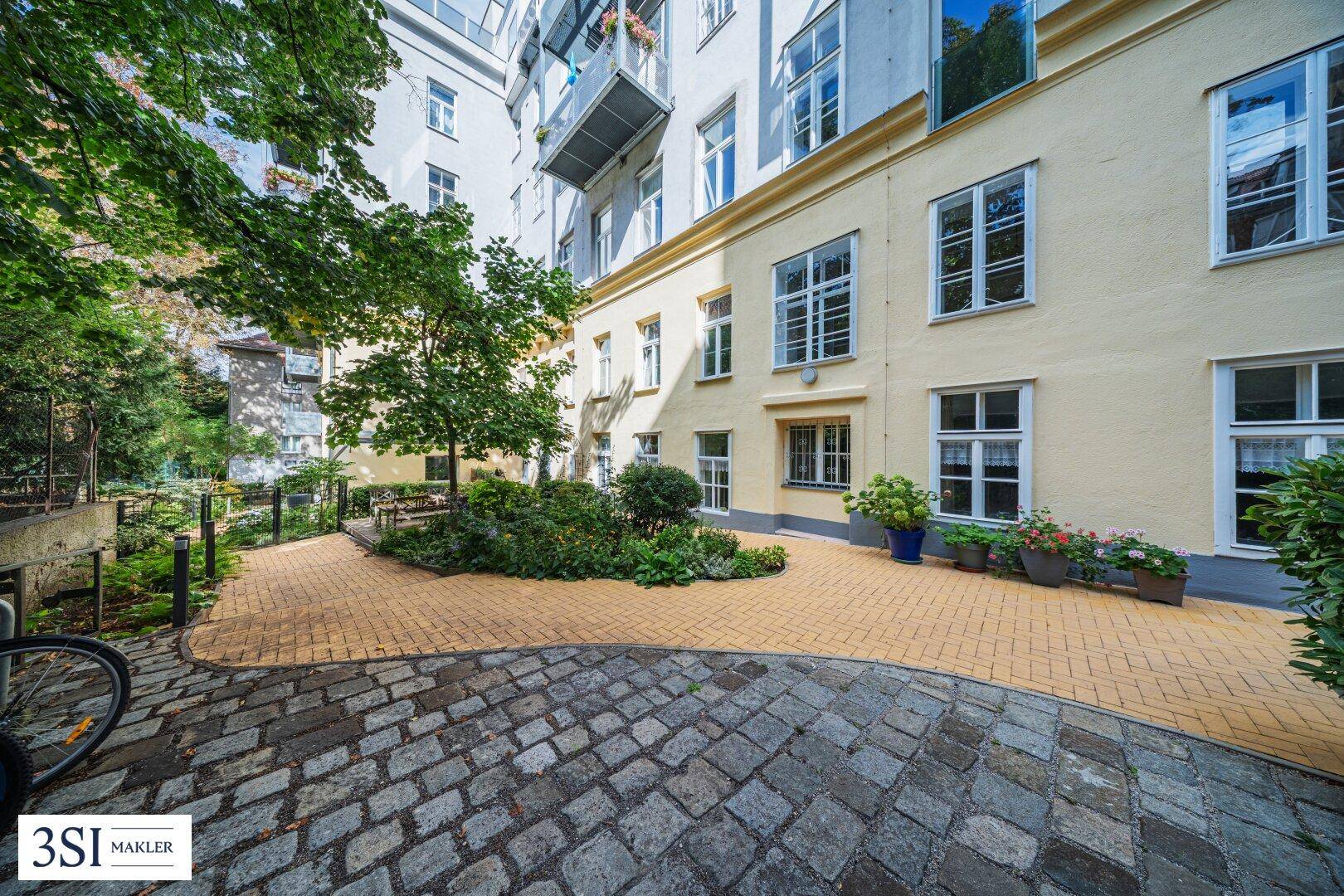 Gepflasterter Innenhof mit Bäumen und Pflanzen, umgeben von Wohngebäuden.