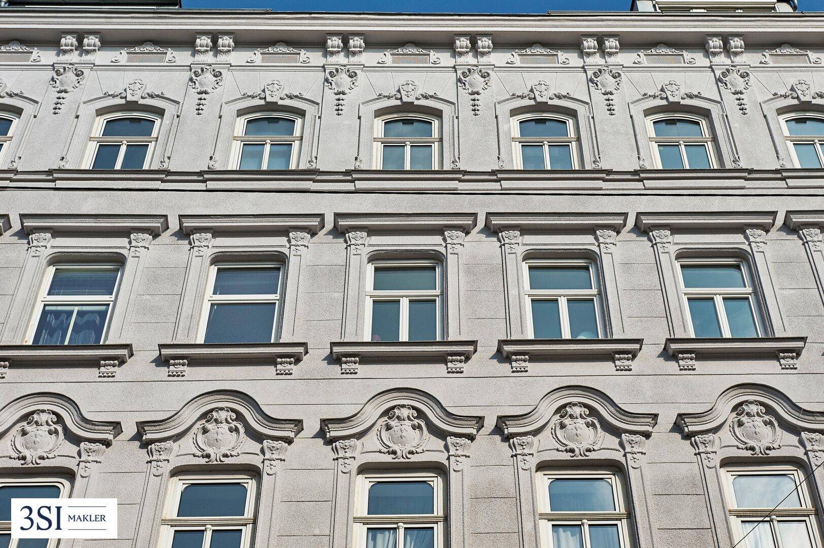 Nahaufnahme der reich verzierten Fassade eines historischen Gebäudes mit vielen Fenstern.