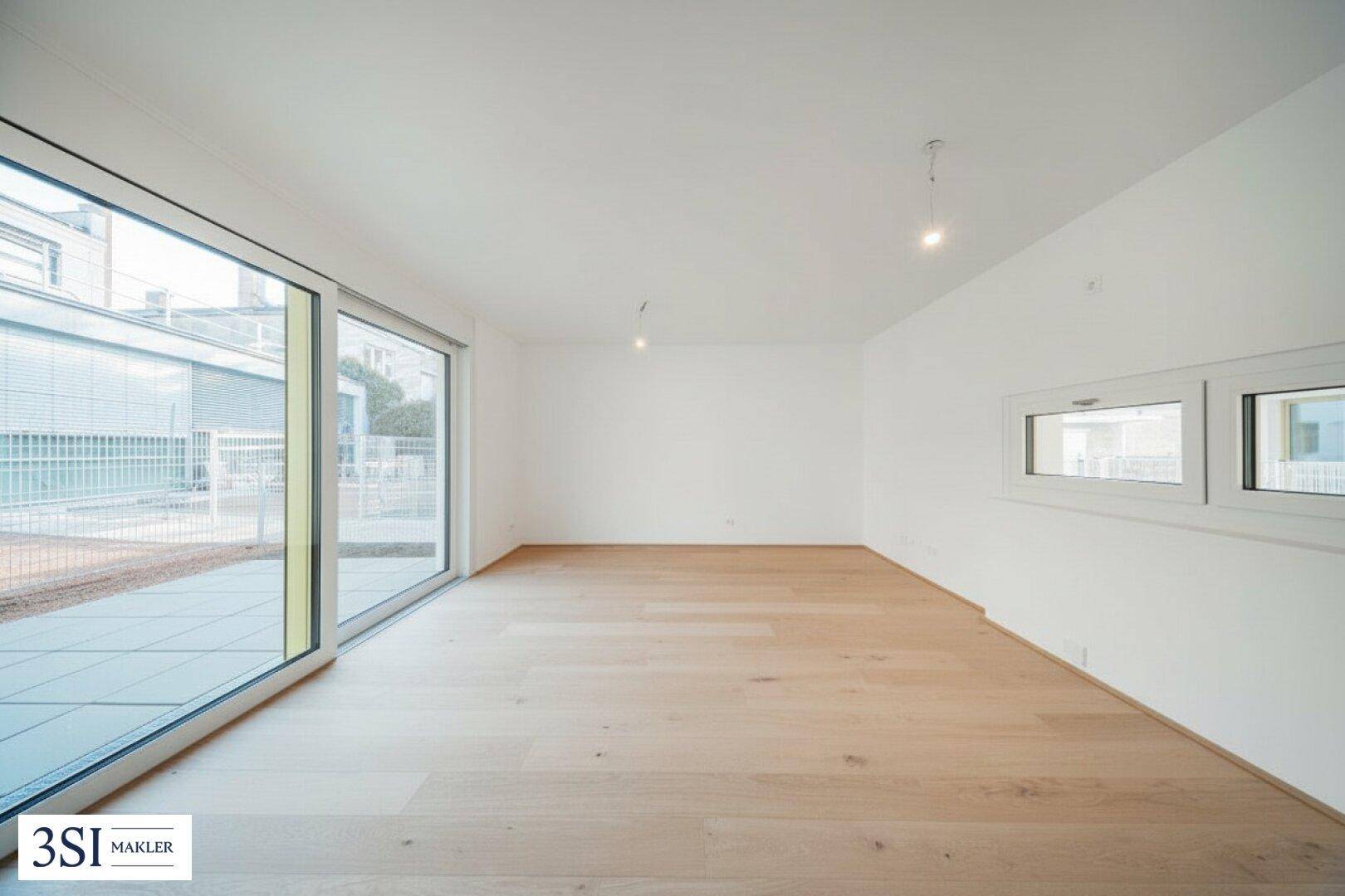Geräumiger, heller Wohnbereich mit großen Fenstern und Holzboden, ideal für individuelle Gestaltung.