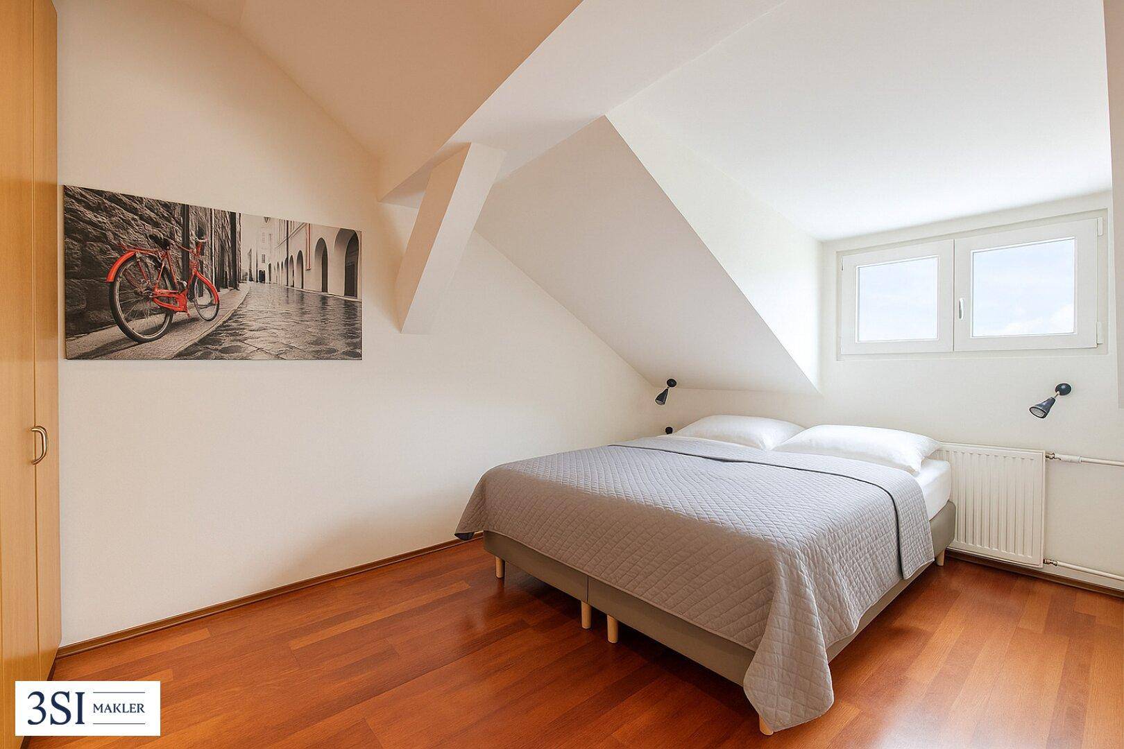 Helles Schlafzimmer im Dachgeschoss mit Holzboden und gemütlichem Bett.