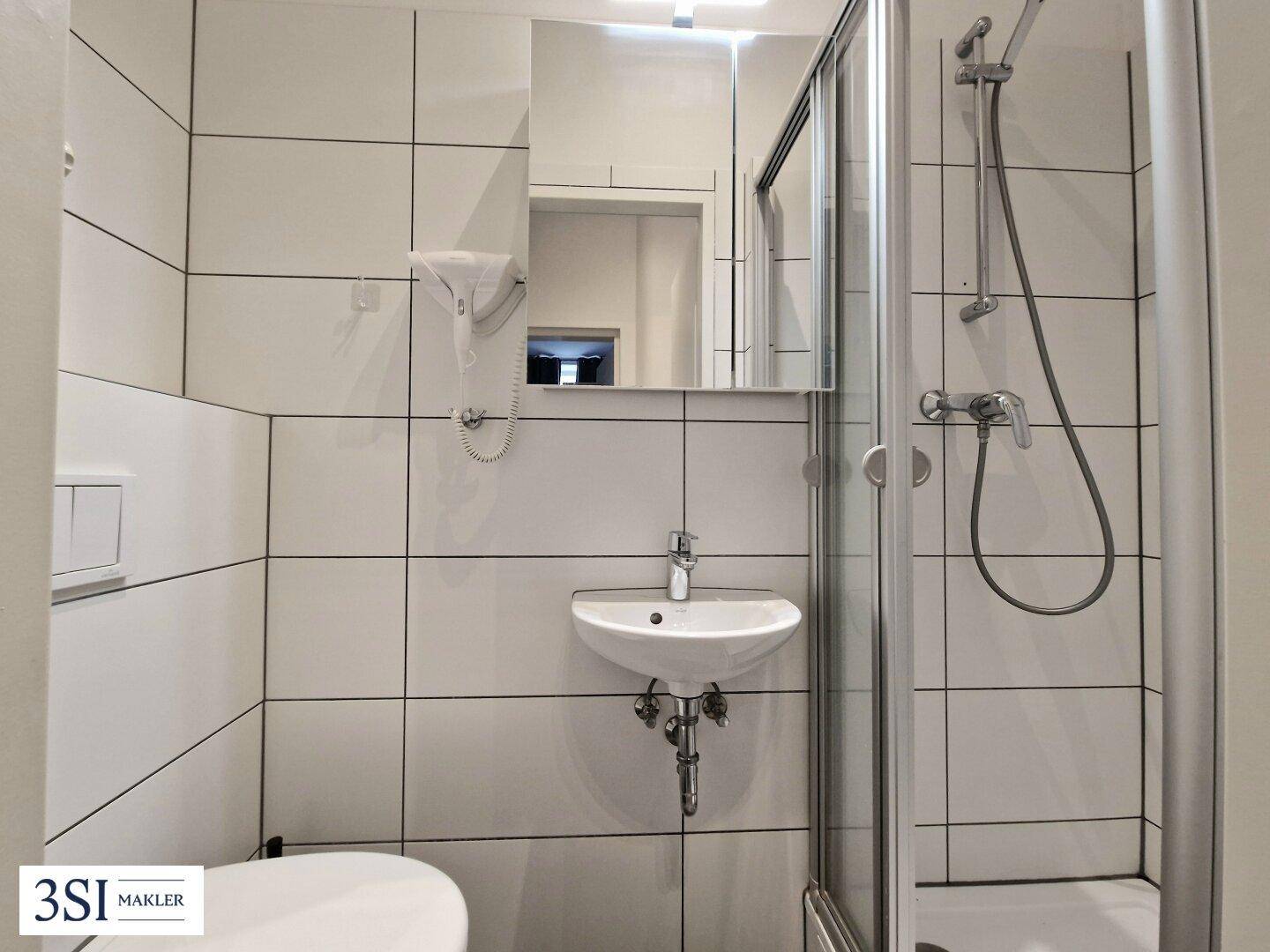Modernes Badezimmer mit weißen Fliesen, Duschkabine und einem einzelnen Waschbecken.