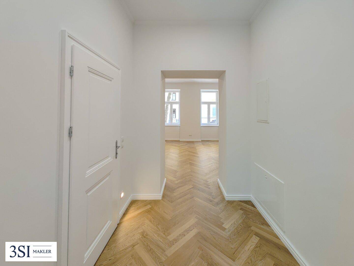 Langer, heller Flur mit Fischgrätparkett, der den Blick in ein weiteres Zimmer freigibt.