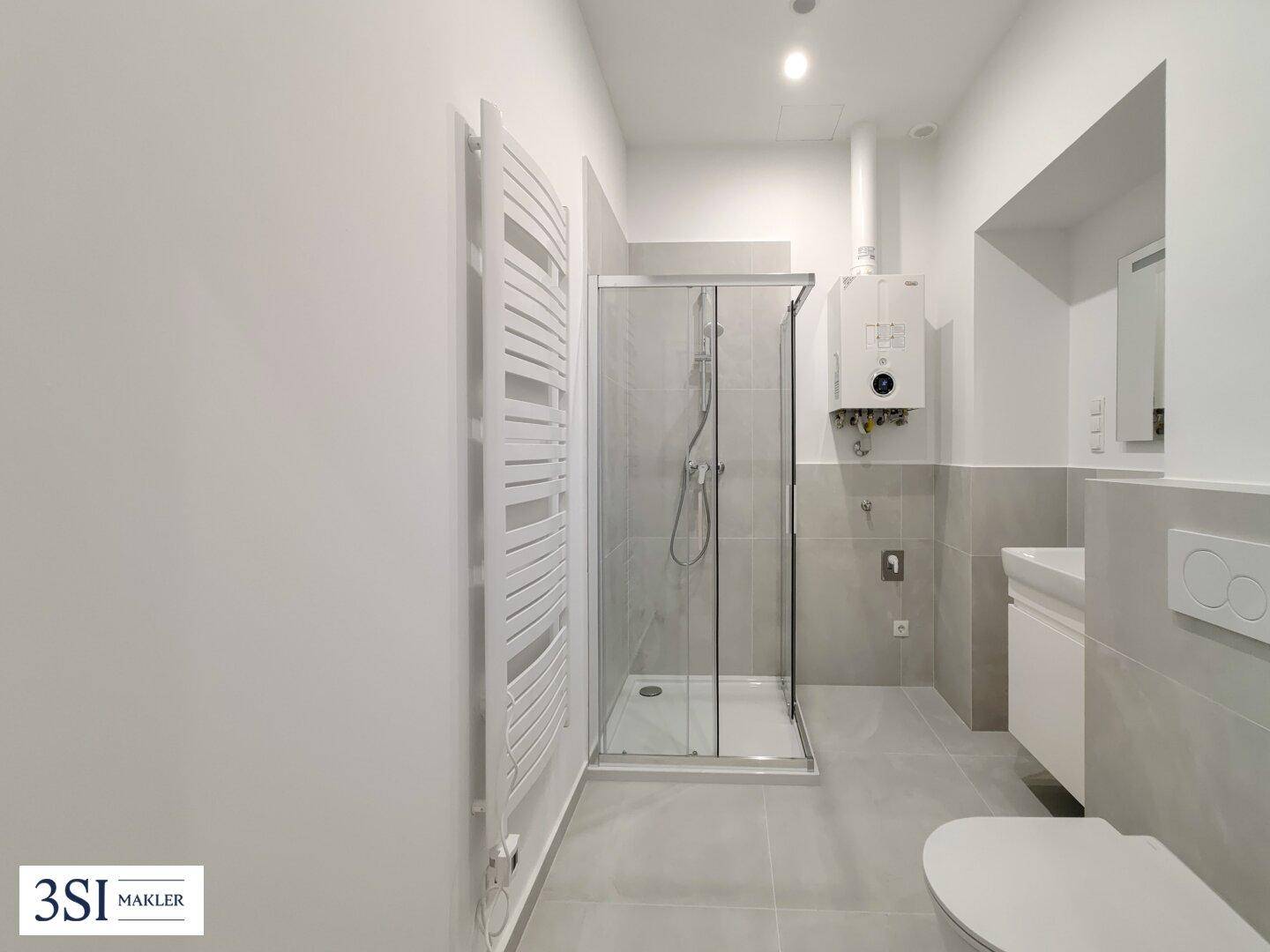 Modernes Badezimmer mit Duschkabine, beheiztem Handtuchhalter und hellgrauen Fliesen.