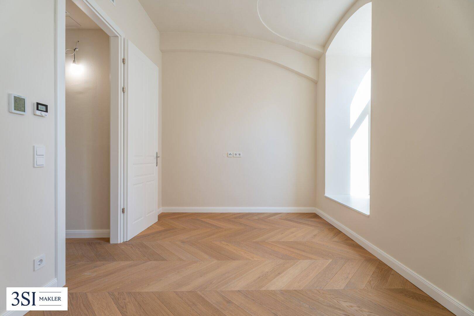 Heller Raum mit elegantem Fischgrätparkett und einem großen, bogenförmigen Fenster.