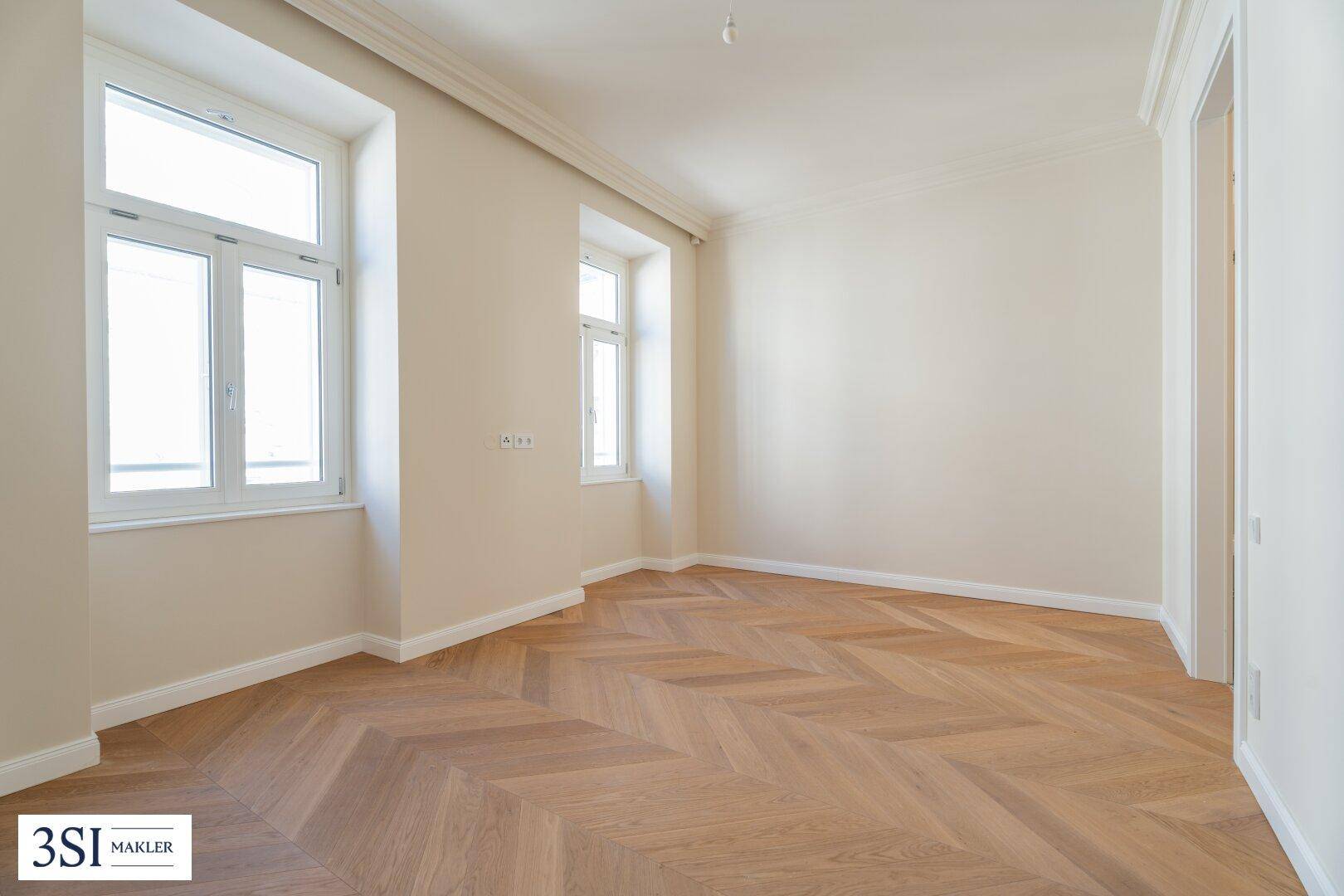 Lichtdurchfluteter Raum mit elegantem Fischgrätparkett und hohen Fenstern, der vielseitig nutzbar ist.