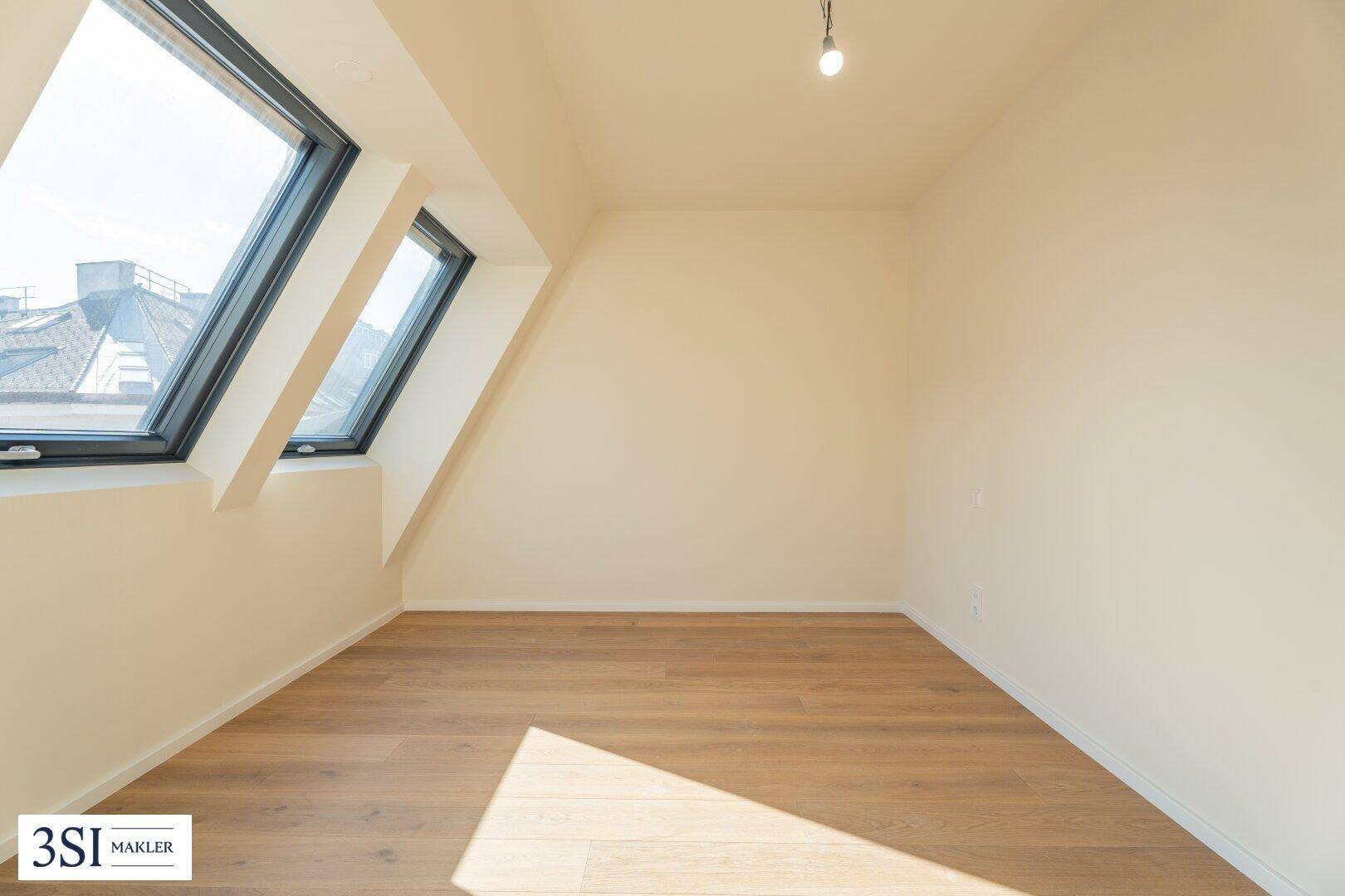 Helles Zimmer im Dachgeschoss mit Holzboden und zwei großen Dachfenstern.