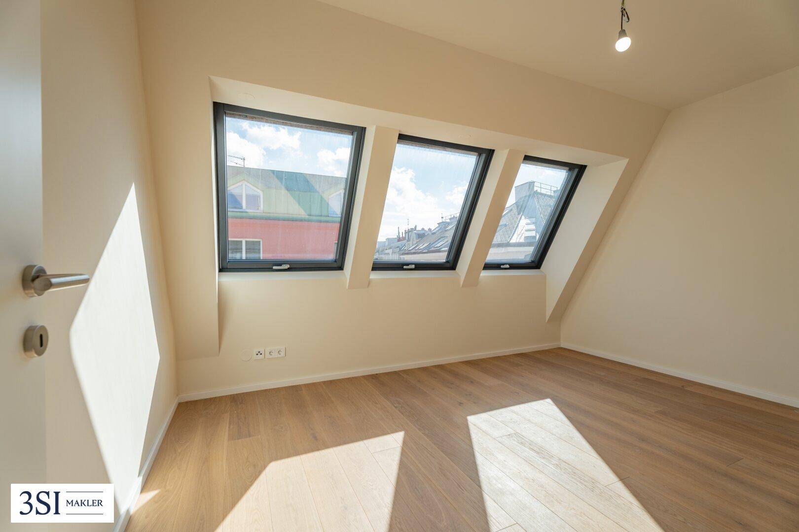 Lichtdurchflutetes Zimmer mit Parkettboden und drei modernen Dachfenstern, ideal als Schlafzimmer.
