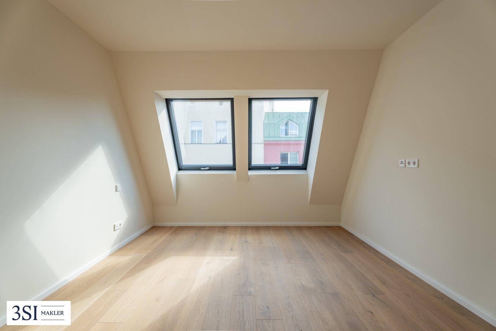 Helles Dachgeschosszimmer mit zwei großen Dachfenstern und Holzboden.