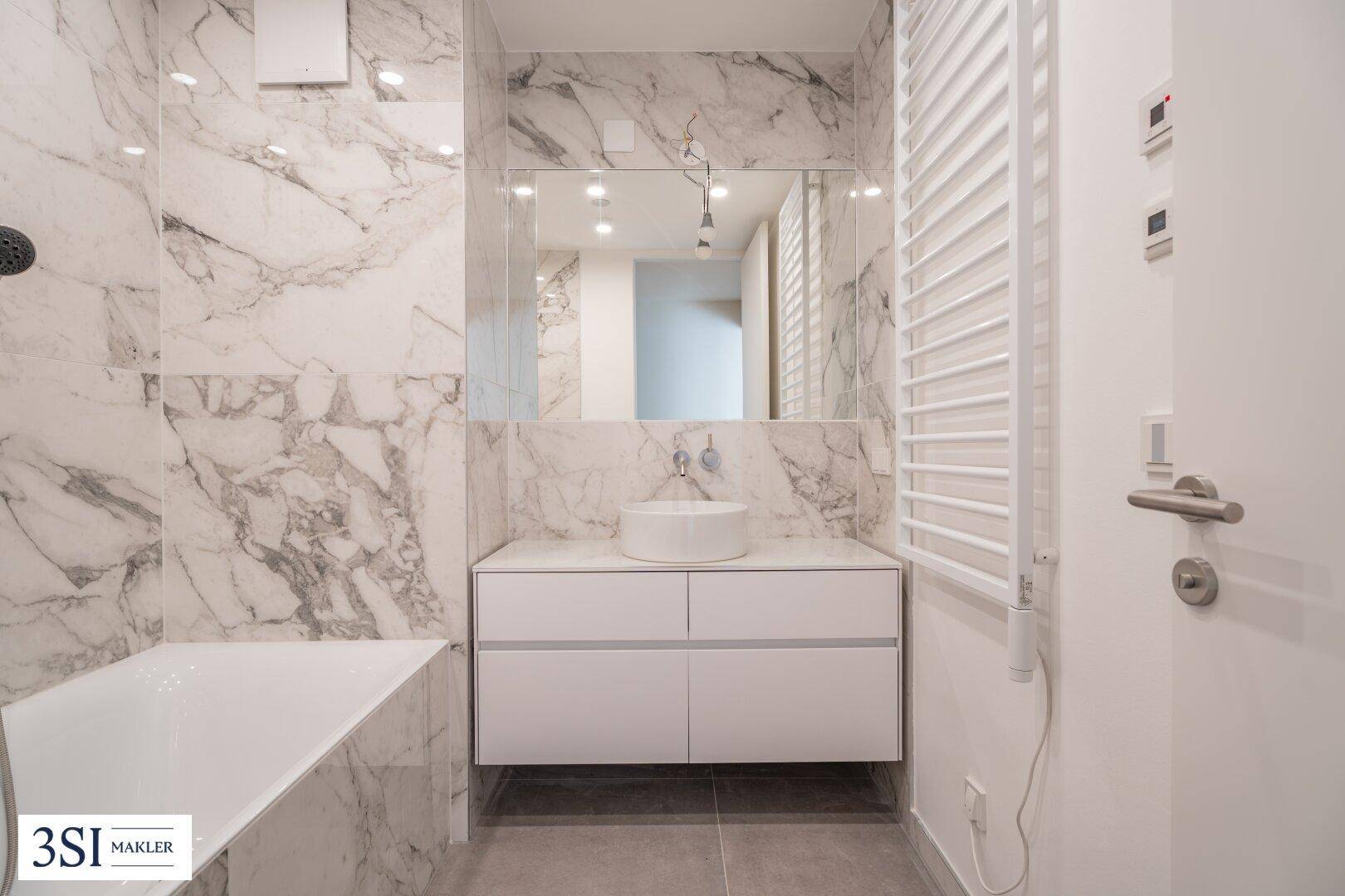 Elegantes Badezimmer mit Marmorfliesen, moderner Waschtischplatte und Badewanne.