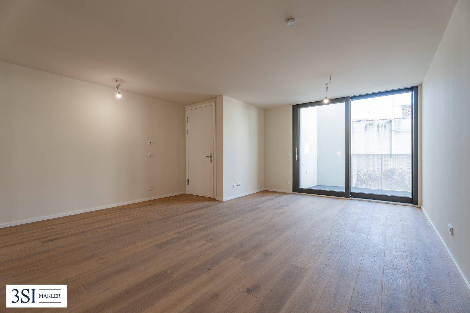 Helles, leeres Zimmer mit Holzboden und Zugang zu einem Balkon, ideal für Wohn- oder Schlafbereich.