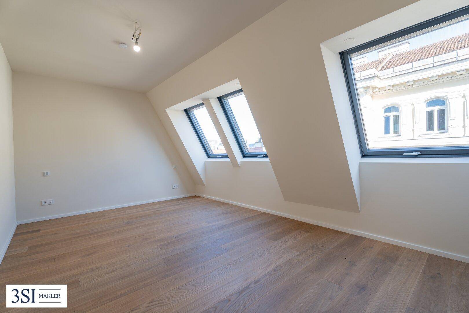 Heller Raum im Dachgeschoss mit Holzboden und schrägen Wänden, ausgestattet mit Dachfenstern und Stadtblick.