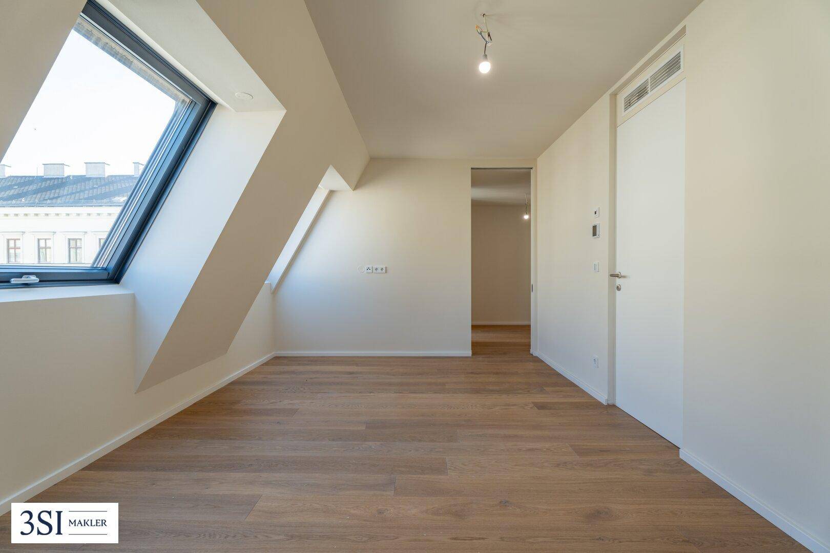 Dachgeschosszimmer mit Holzboden, schrägen Wänden und einem großen Dachfenster, bietet viel Licht und Zugang.