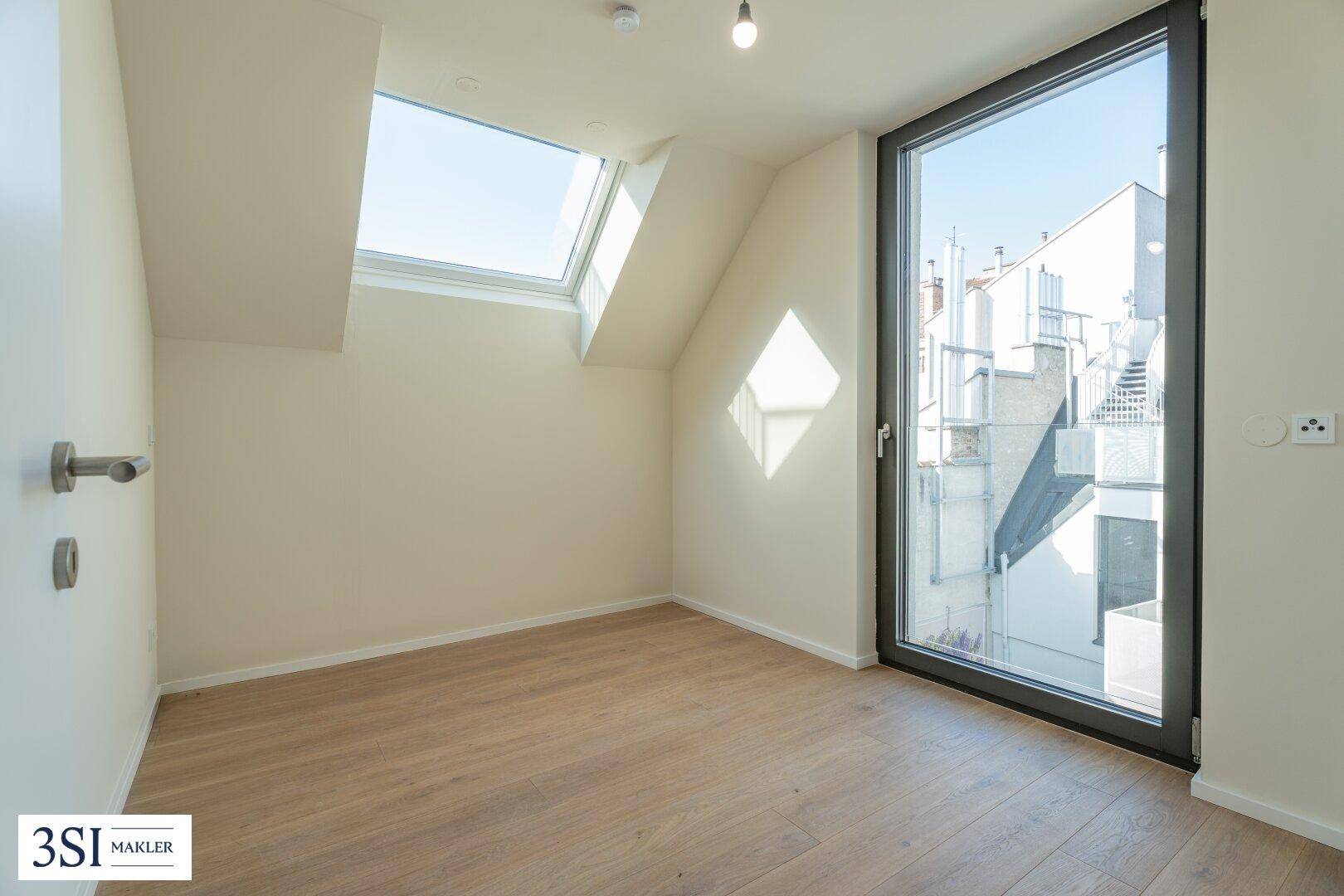 Heller Raum mit Holzboden, einem hohen Fenster und einem zusätzlichen Dachfenster für viel Tageslicht.