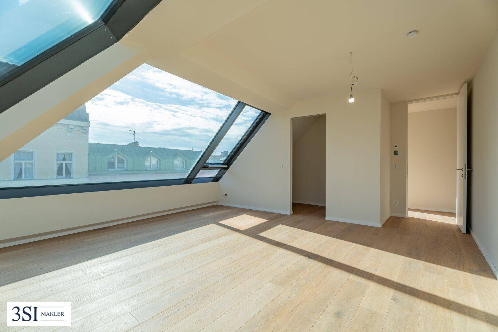 Geräumiges Zimmer mit schrägen Dachfenstern und hellem Holzboden, bietet viel natürliches Licht.