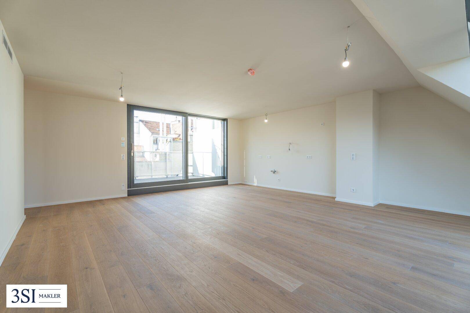 Geräumiges Zimmer mit Holzboden und großer Schiebetür, die zu einem Balkon führt.