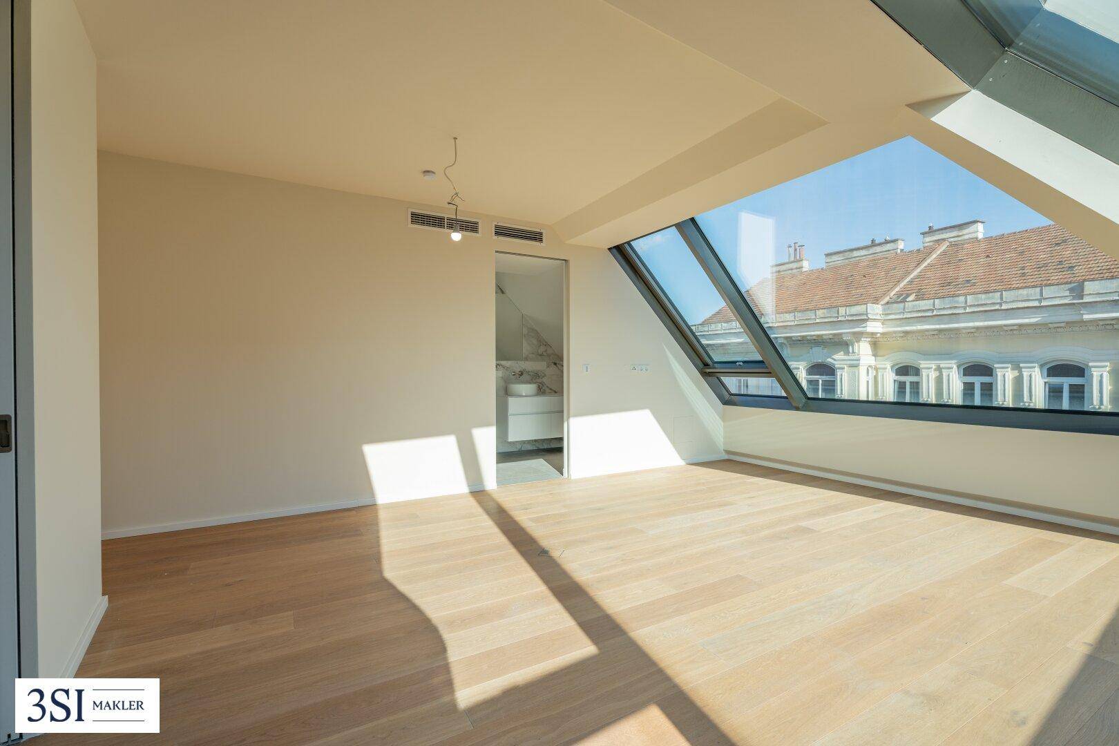 Heller Wohnraum mit Holzboden und schrägen Fenstern, angrenzend an ein modernes Badezimmer.