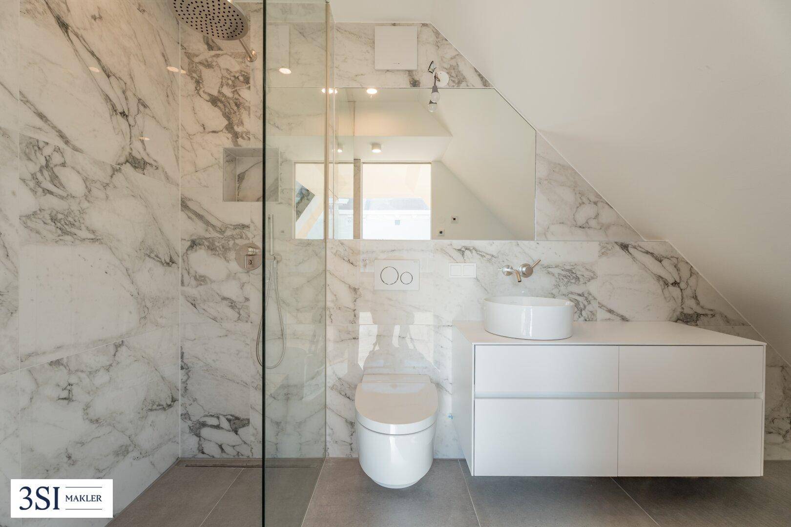Modernes Badezimmer mit Marmorfliesen, begehbarer Dusche und wandhängendem WC unter Dachschräge.