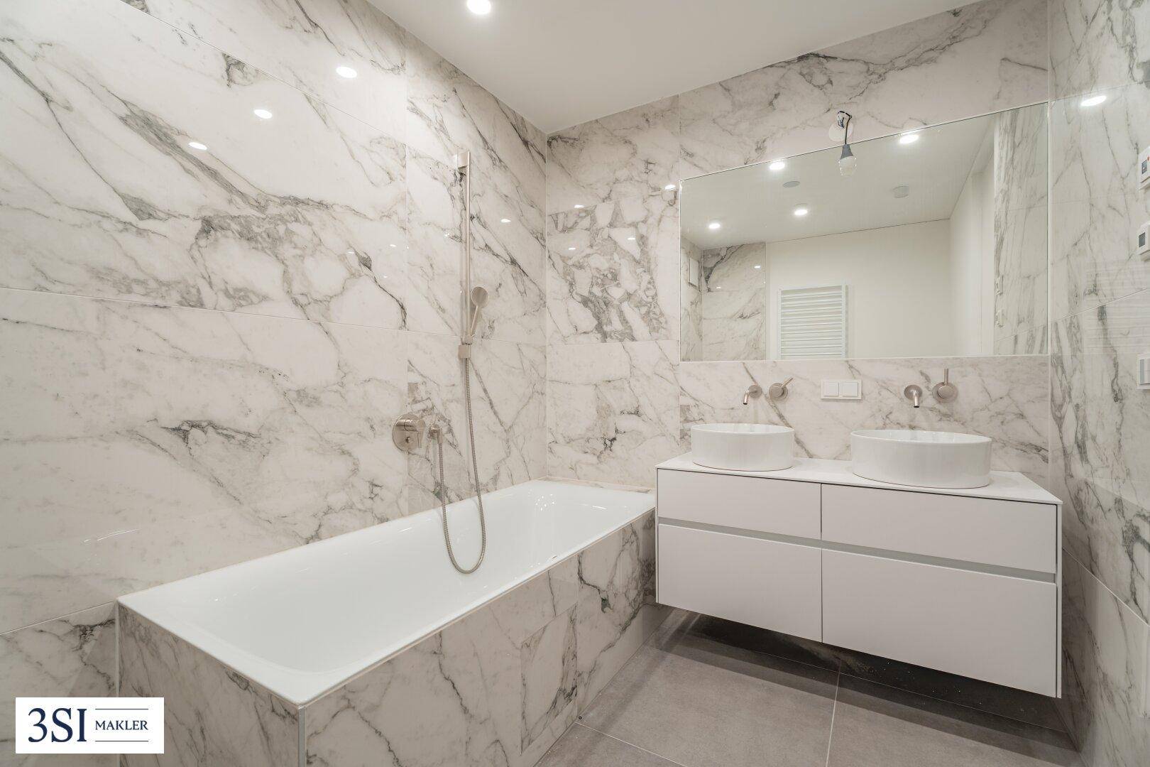 Elegantes Badezimmer mit Marmorfliesen, Badewanne und Doppelwaschbecken, sehr hell.