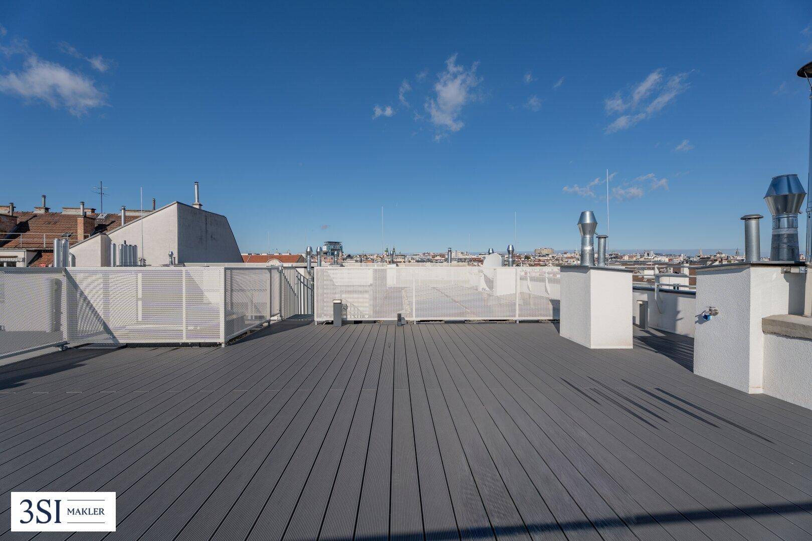 Große Dachterrasse mit Holzdielenboden und weitem Blick über die Dächer der Stadt.