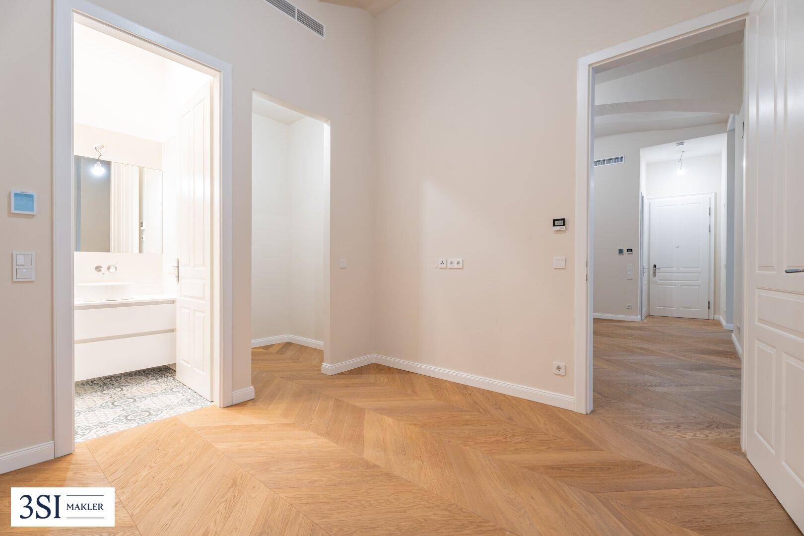 Heller Durchgangsbereich mit Fischgrätparkett und Blick in ein modernes Badezimmer.
