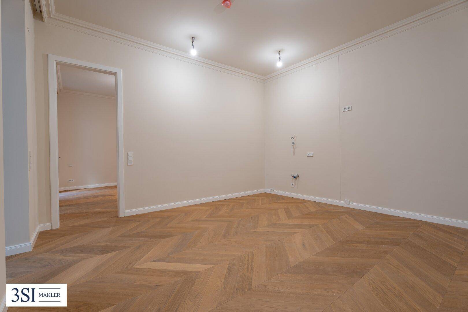 Geräumiger, unmöblierter Raum mit elegantem Fischgrätparkett und hohen Decken.